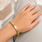Minimal gold bangle bracelet with green and pink gemstone accents